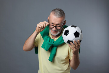 Portrait of handsome senior man with soccer ball on grey background