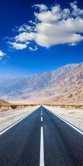 Naklejka premium A vast desert road stretches into the horizon, framed by majestic mountains and a vibrant blue sky.
