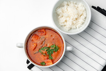 Bowl of curry with pieces of meat and a side of steamed rice arranged neatly for a meal