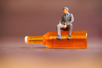 Miniature Man Sitting on an Empty Beer Bottle on Wooden Table Background