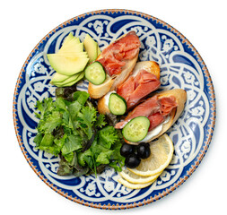 Colorful plate of smoked salmon sandwiches with cucumbers, greens, and olives on a decorative blue platter