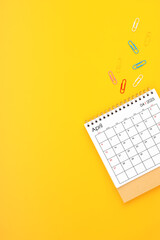 April 2025 desk calendar and paper clips on yellow background. Position with copy space.