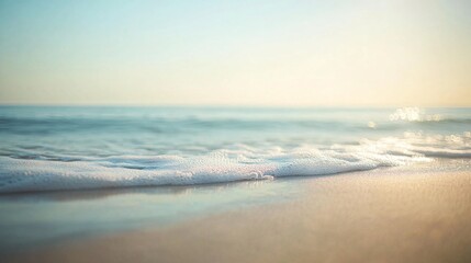 Obraz premium 2410_121.close-up of a calm ocean shoreline, gentle waves lapping onto a smooth sandy beach, the water sparkling under soft sunlight, a blurred horizon in the distance with hints of blue sky and sea,
