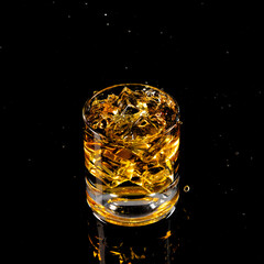 Glass of whiskey with ice cubes on black background. As whiskey is poured from the bottle into the glass