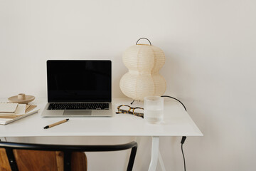 Functional workspace with modern laptop and notebooks on white desk with artistic paper lamp