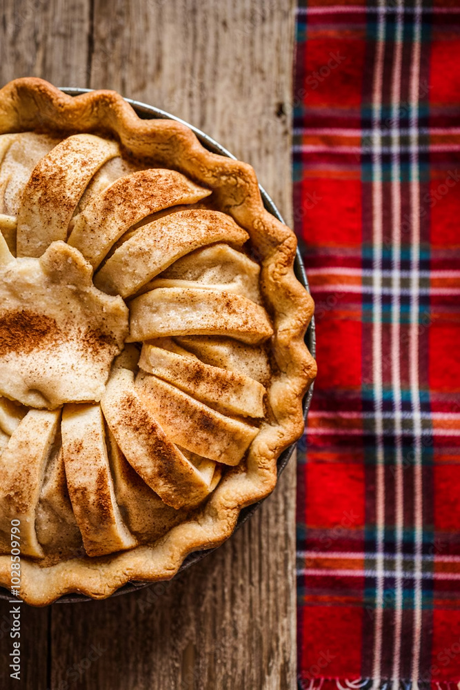Poster apple pie with cinnamon on a wooden table with a red cloth, top view