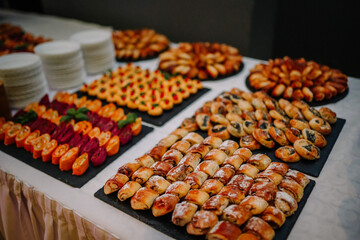 A table spread with various pastries and appetizers, including stuffed rolls, pinwheels, and savory bites, displayed on black platters, ready for a buffet..