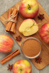 Red apple, cinnamon sticks and cinnamon in bowl on grey concrete background. Vertical photo
