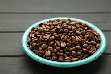 Coffee beans on plate on black background. Space for text