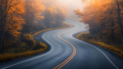 Naklejka premium An empty, winding road winds through the woods on an autumn morning, shrouded in fog. The trees are adorned with leaves in various shades of orange and brown. 