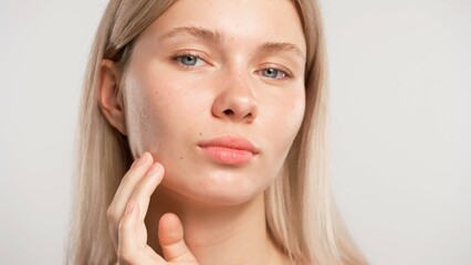 Obraz premium Young blonde woman posing at camera touching face line with hand, isolated on white studio background close up shot. Beauty skin care concept