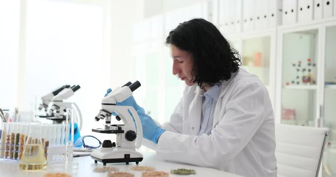 Scientist examines glass test tubes with various cereals on microscope in agricultural laboratory. Young agronomist scientist doing research