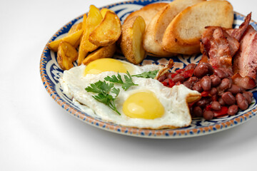 Delicious breakfast plate featuring eggs, beans, bacon, and potato wedges served on a decorative dish