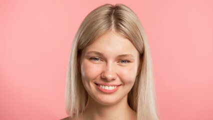 Young blonde woman posing at camera, smiling happy face expression, isolated on pink studio background close up shot. Beauty skin care concept