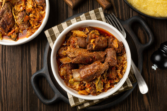 Top view of cassoeula is a typical winter dish popular in western Lombardy, Milanese, North Italian dish. Main ingredients are Savoy cabbage, pork ribs, italian sausage. Polenta. Dark wooden table..