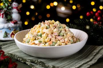 Russian salad Olivier on a Christmas or New Year table. Made with vegetables, mayonnaise,  peas, mortadella sausage and eggs served in a white bowl.