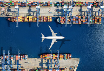 Aerial top view of a cargo plane flying above container freight port with docked ships and loading and unloading by cranes and trucks © moofushi
