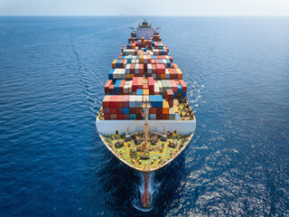 Aerial front view of a big cargo container carrier ship sailing over the ocean with speed