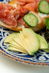 Colorful plate of smoked salmon sandwiches with cucumbers, greens, and olives on a decorative blue platter