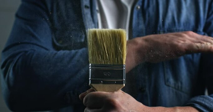 Super slow motion close up of paintbrush being touched by house painter with splashes of color and water isolated on soft background at 1000 fps.