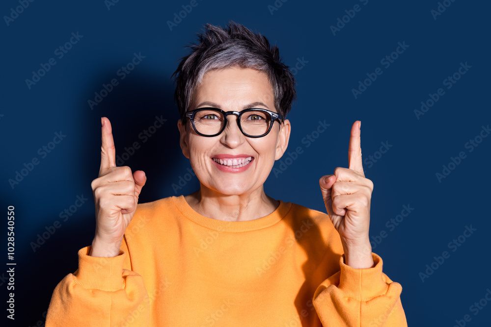 Poster Photo portrait of attractive mature woman point up empty space dressed stylish yellow clothes isolated on dark blue color background