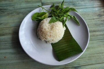 White rice and basil leaves are placed on banana leaves and placed on a white plate, with a close-up view.