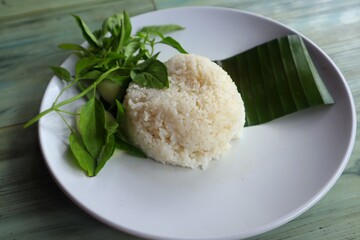 White rice and basil leaves are placed on banana leaves and placed on a white plate, with a close-up view.