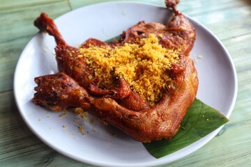 Whole fried duck with crunchy topping on top on a white plate close up view.
