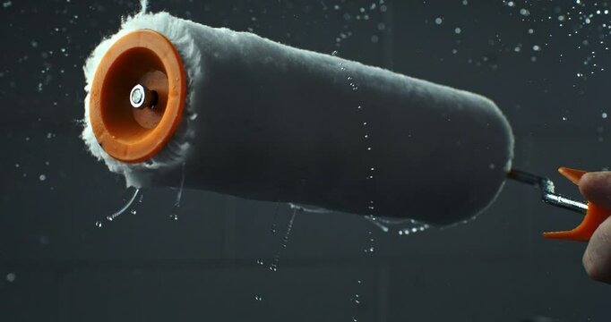 Super slow motion macro of paint roller is being spinned with splashes of color and water isolated on soft background at 1000 fps.