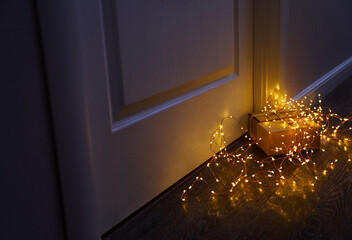 Wrapped gift box with fairy lights at a doorway in dim light