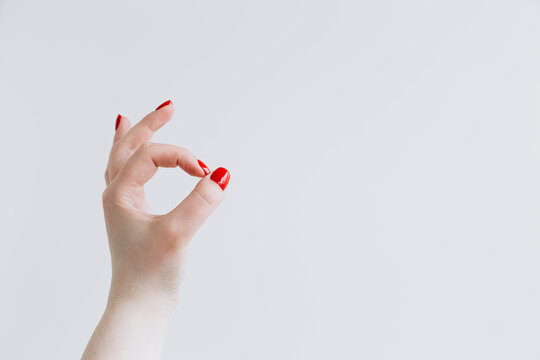 Female hand with red nails forming okay sign on white background