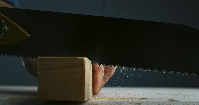 Super slow motion macro of artisan carpenter is working wood with hacksaw with flying wood sawdust on workbench in workshop at 1000 fps.