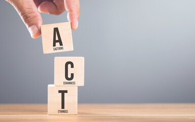 A hand arranging wooden blocks with the letters A, C and T on a table, set against a gray. Symbolizes the process of taking action to implement changes in various aspects of life or business
