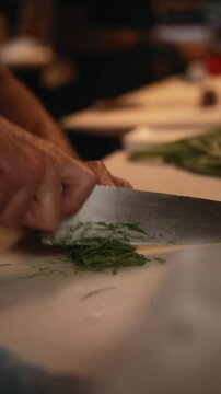 Vertical closeup footage of a chef chopping fresh green herbs with sharp knife on a kitchen counter
