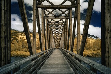 Fototapeta premium Wooden bridge leading to mountains under a cloudy sky