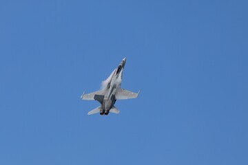 Military jet aircraft in vertical climb against clear blue sky.