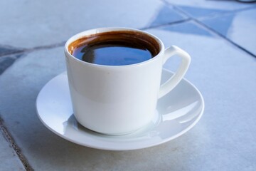 Close-up shot of a cup of black coffee in a white cup and saucer on a tiled surface