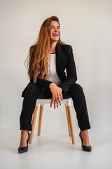 Young woman in a black suit laughing joyfully while sitting.