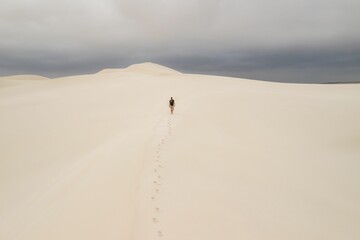 Lone person walking on sand dunes under a cloudy sky.