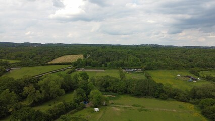 Aerial view of green fields and forest under cloudy sky.