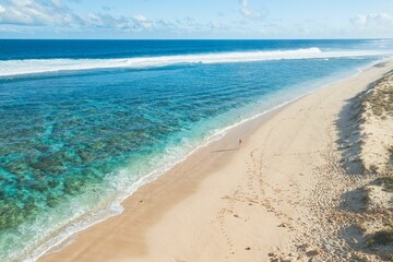 Aerial view of a person walking along a pristine beach with blue waters and cliffs on a sunny day