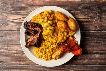 Plate of grilled chicken, macaroni and cheese, corn, hush puppies, and lobster tail.