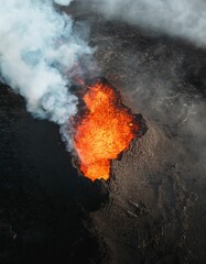 Aerial view of an erupting volcano with glowing lava and smoke. © Wirestock