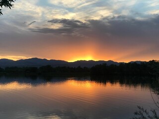 Naklejka premium Sunset over a calm lake with mountains.