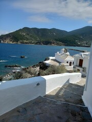 Obraz premium White-Washed Buildings by the Sea with Mountain Backdrop in Greece