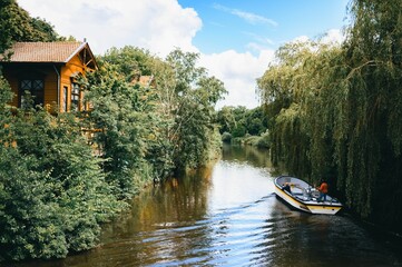 Naklejka premium Serene river scene with a boat and a wooden house surrounded by lush greenery. Amsterdam