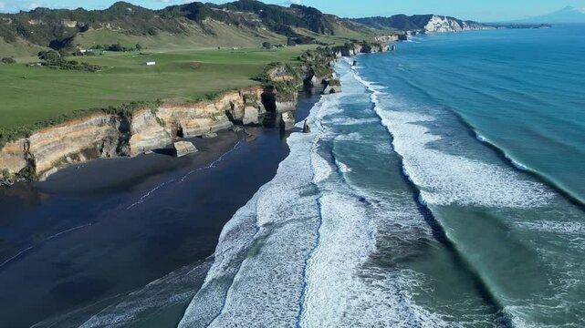 Drone view of the sea waves with green rocky shore at the Three Sisters Lookout, on a sunny day