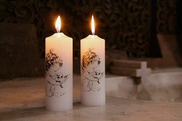 Lit candles with cherub designs on marble.