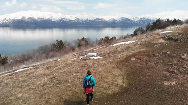 Aerial view of a woman traveler walking along the shore of Lake Sevan in Armenia with snow mountains The scene highlights peaceful exploration and the stunning natural beauty of the region