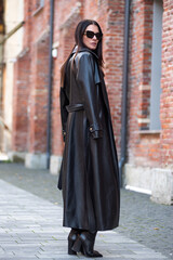 Beautiful woman wearing long leather coat, walking on the street